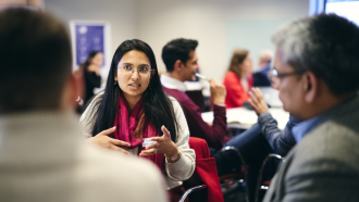 Sugandha Srivastav Sugandha Srivastav wearing a pink scarf and talking to other conference attendees.