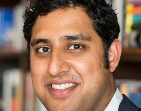 Rajiv Joshi Rajiv Joshi smiling in front of a bookcase.