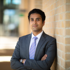 Akshay Mangla Akshay Mangla standing in the SBS hallway wearing a grey suit and smiling.