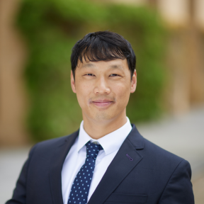 Kevin Tang standing in the SBS hallway wearing a navy suit and smiling. 