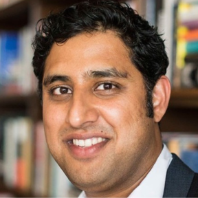 Rajiv Joshi Rajiv Joshi smiling in front of a bookcase.